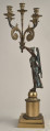 Kandelabr z uskrzydloną postacią na postumencie przymającą w rękach ramiona świecznika.Bok prawy