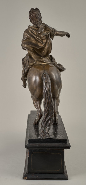 Brązowy posążek na drewnianym postumencie przedstawia Ludwika XIV siedzącego na wspiętym koniu, w stroju i pozie rzymskiego imperatora, w peruce na głowie.