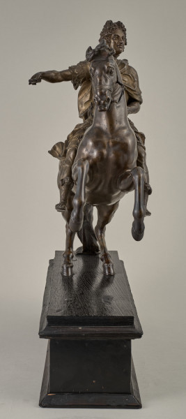 Brązowy posążek na drewnianym postumencie przedstawia Ludwika XIV siedzącego na wspiętym koniu, w stroju i pozie rzymskiego imperatora, w peruce na głowie.