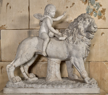 Amorek na lwie. Rzeźba marmurowa przedstawia kroczącego lwa z siedzącym na niej amorkiem na tle kamiennej ściany.