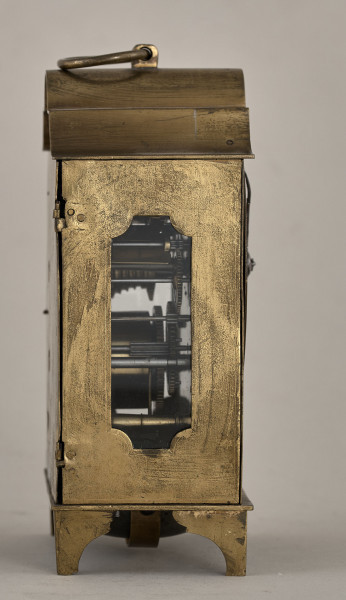 Boczna, złocona ścianka zegara ze szklonym otworem ukazującym mechanizm.