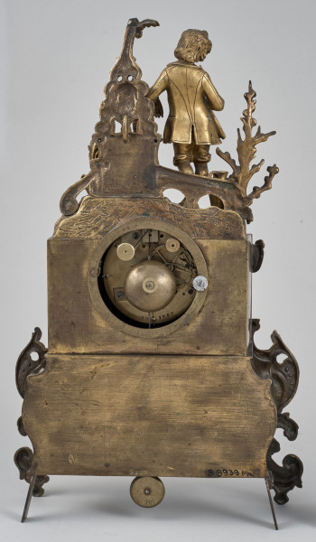 ﻿Zegar kominkowy wykonany z brązu, wsparty na czterech nóżkach. Tył zegara ze ścianką bez dekoracji i otworem dostępowym do mechanizmu.
