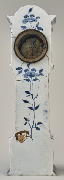 Zegar na białym cokole ceramicznym z niebieskimi holenderskimi przedstawieniami wiatraków w typie Delft.  Tylna ścianka zegara dekorawana motywem roślinnym. W górnej części otwór na mechanizm.