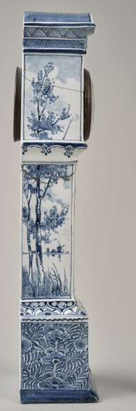 Zegar na białym cokole ceramicznym z niebieskimi holenderskimi przedstawieniami wiatraków w typie Delft. Bok prawy
