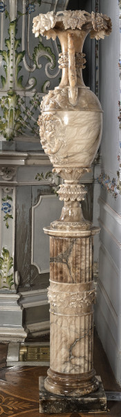 Wazon alabastrowy bogato rzeźbiony motywami roślinnymi stojący na kolumnie.