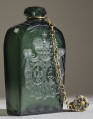 Flasza z zielonego szkła z herbem Trąby i Waga. Widoczny złoty łańcuszek z korkiem.