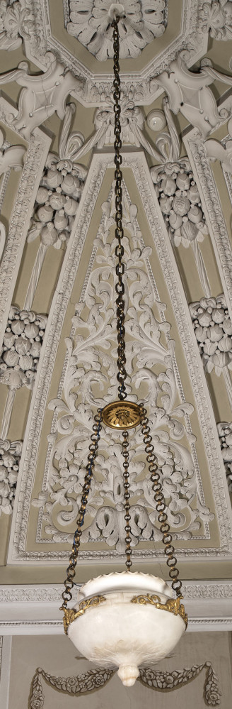 Ampla wisząca na łańcuchu połączonym z talerzem, z którego odchodzą 3 kolejne łańcuchy. z rzeźbionego alabastru, ornamenty i łańcuchy z brązu pozłacanego. Ujęcie na tle bogato dekorowanego sklepienia.