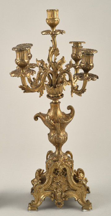 Kandelabr. Stojący świecznik w kolorze złotym, bogato dekorowany ornamentem ażurowym roślinnym.