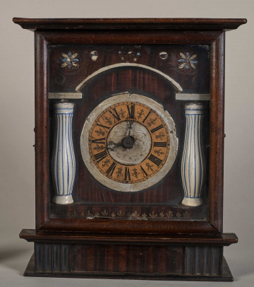 Przód zegara w formie drewnianej skrzynki z tarczą pomiędzy dwoma białymi kolumnami