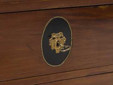 zbliżenie na dekorację szuflad dolnych z owalem pośrodku malowanym na czarno, obwiedzionym perełkowaniem oraz na okucia przy zamkach z elementami architektonicznymi i szarfą