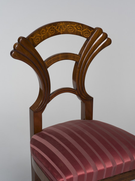 zbliżenie na opracie w kształcie wachlarza ze zdobieniem (intarsjowane gałązki tworzące symetryczne arabeski złączone pośrodku stylizowanym motywem liry) oraz na tapicerowane siedzisko krzesła obite malinowym jedwabiem w paski