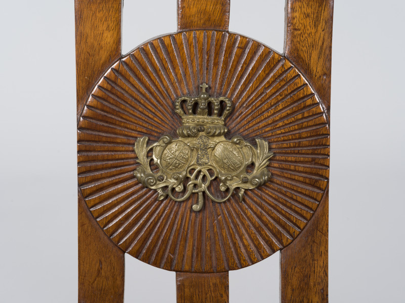 zbliżenie na okrągłą tarczę promieniście żłobkowaną z plakietką brązową w środku, zdobiącą lewą stronę oparcia