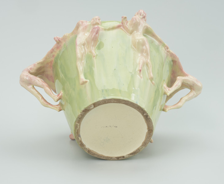 ceramika - Ujęcie z dołu; Wazon z kręgiem postaci. Widoczne postacie od dołu kremowo-różowe na zielonym tle malowanego wazonu.