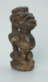rzeźba; przedmiot obrzędowy; Figura kultu sił wegetacji - Ujęcie z przodu z prawej strony. Rzeźbiona w grafitowym steatycie, siedząca na owalnej podstawie, postać ludzka, którą od tyłu obejmuje postać zoomorficzna o cechach jaszczurki.