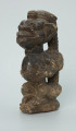 rzeźba; przedmiot obrzędowy; Figura kultu sił wegetacji - Ujęcie z przodu z lewej strony. Rzeźbiona w grafitowym steatycie, siedząca na owalnej podstawie, postać ludzka, którą od tyłu obejmuje postać zoomorficzna o cechach jaszczurki.