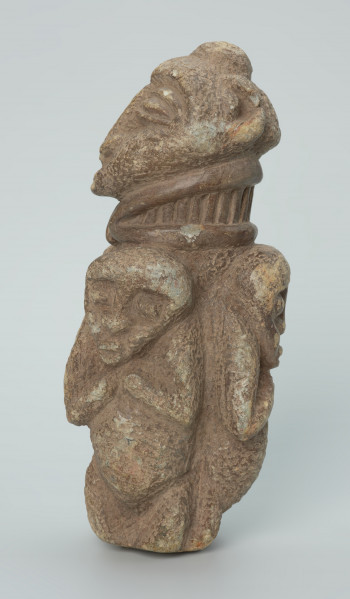 rzeźba; przedmiot obrzędowy; figura kultu zmarłych - Ujęcie lewy bok. Rzeźbiona w szarobeżowym steatycie, otoczona trojgiem dzieci, postać ludzka o cechach kobiecych z naszyjnikiem przypominającym kryzę.