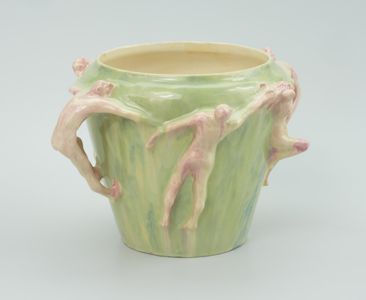 ceramika - Ujęcie z boku; Malowane postacie ceramiczne przyczepione do wazonu. Postać męska na wprost ciągnąca przez postać męską z lewej strony za rękę. Z prawej strony wazonu widoczna postać żeńska ze zgiętym prawym kolanem.