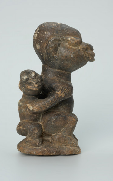 rzeźba; przedmiot obrzędowy; Figura kultu sił wegetacji - Ujęcie prawy bok. Rzeźbiona w grafitowym steatycie siedząca postać ludzka o cechach kobiecych z podkurczonymi nogami i dzieckiem na plecach.