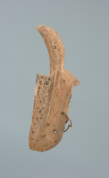 maska zająca - Ujęcie z lewego boku. Drewniana, rzeźbiona maska w kształcie zająca, którego  uszy wygięte są do przodu i wydrążone.