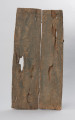 drzwi - Ujęcie z tyłu. Drzwi drewniane do spichlerza, składające się z dwóch części połączonych klamerkami z żelaznej blachy. Zdobione płaskorzeźbionymi postaciami o schematycznych rysach z dłońmi na kolanach. Postaci w pięciu poziomych rzędach po 12 i 13 w rzędzie. Na wysokości czwartego rzędu przymocowana z lewej strony nieruchoma część zasuwy, wykonana z drewna i zdobiona rzeźbioną siedzącą postacią. Ruchomej części zasuwy brak.