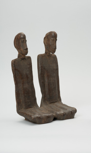 drewniana figura - Ujęcie z przodu, z lewej strony. Para przodków siedzących obok siebie, ręce przylegające wzdłuż tułowia.