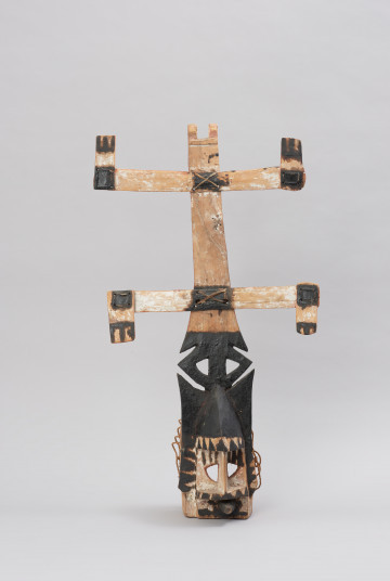 rzeźbiona maska - Ujęcie z przodu. Drewniana, rzeźbiona maska, do której przymocowany jest skorzany sznurek.