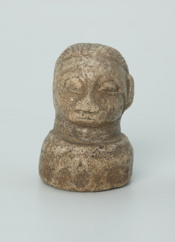 rzeźba; przedmiot obrzędowy; Głowa - Ujęcie z przodu. Rzeźbiona w szarobeżowym steatycie głowa ludzka na okrągłej podstawie z charakterystycznym uczesaniem lub nakryciem głowy w formie płaskiego ornamentu kostkowego.