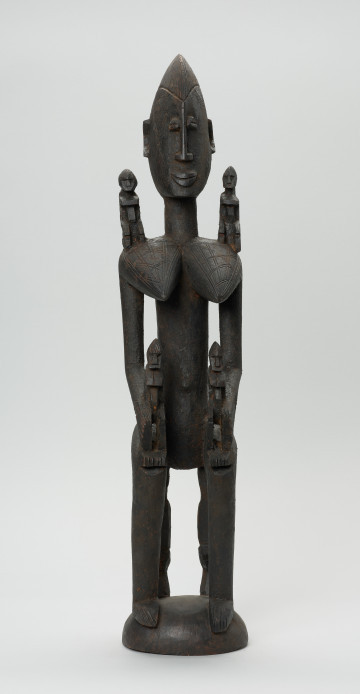 drewniana figura - Ujęcie z przodu. Drewniana, rzeźbiona figura kobiety. Na jej ramionach i rękach znajdują się mniejsze figurki.