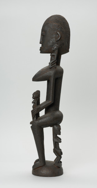 drewniana figura - Ujęcie z prawego boku. Drewniana, rzeźbiona figura kobiety. Na jej ramionach i rękach znajdują się mniejsze figurki.