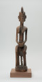 drewniana figura - Ujęcie z przodu. Drewniana, rzeźbiona figura kobiety, siedzącej na stołku.