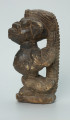 rzeźba; przedmiot obrzędowy; Figura kultu sił wegetacji - Ujęcie lewy bok. Rzeźbiona w grafitowym steatycie, siedząca na owalnej podstawie, postać ludzka, którą od tyłu obejmuje postać zoomorficzna o cechach jaszczurki.