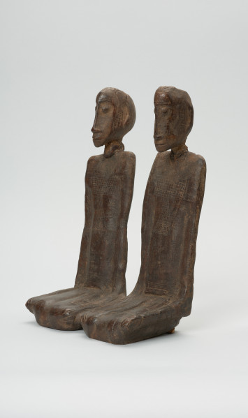 drewniana figura - Ujęcie z przodu, z prawej strony. Para przodków siedzących obok siebie, ręce przylegające wzdłuż tułowia.