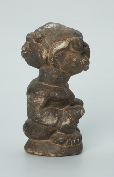 rzeźba; przedmiot obrzędowy; Figura kultu sił wegetacji - Ujęcie prawy bok. Rzeźbiona w grafitowym steatycie siedząca postać ludzka o dwóch twarzach, z przodu i z tyłu głowy.