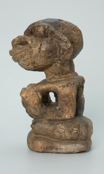 rzeźba; przedmiot obrzędowy; Figura kultu sił wegetacji - Ujęcie lewy bok. Rzeźbiona w białoszarym steatycie siedząca na płaskiej, owalnej podstawie kobieta trzymająca w dłoniach, przy biuście zwrócone ku niej dziecko.