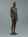 akt męski - Ujęcie z przodu lekkim skosem w prawą stronę; Rzeźba z brązu przedstawiająca nagiego, młodego, szczupłego mężczyznę, stojącego twarzą do widza z rękami wzdłuż ciała.