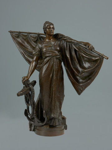 posąg - Ujęcie z przodu; Stojąca młoda kobieta w powłóczystej szacie, z żaglem na lewym ramieniu, z prawą ręką opartą o kotwicę. Rzeźba jest pomniejszoną kopią figury wieńczącej fontannę postawioną w 1895 r. na obecnym placu tobruckim.