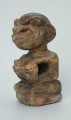rzeźba; przedmiot obrzędowy; Figura kultu sił wegetacji - Ujęcie z przodu z lewej strony. Rzeźbiona w białoszarym steatycie siedząca na płaskiej, owalnej podstawie kobieta trzymająca w dłoniach, przy biuście zwrócone ku niej dziecko.