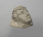 głowa - Ujęcie z góry skosem w prawą stronę; Z nieregularnego bloku szarożółtego kamienia wyłoniona twarz kobieca o grubych rysach, z czołem przykrytym falistymi włosami.