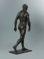 akt męski - Ujęcie z tyłu; Rzeźba nagiego mężczyzny. Głowa lekko pochylona w lewą stronę, ręce opuszczone wzdłuż tułowia, lewa noga lekko wysunięta do przodu tak, jakby mężczyzna stawiał krok do przodu.