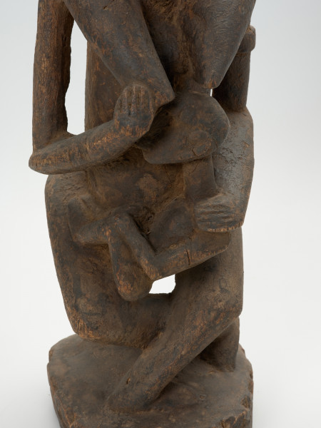 drewniana, rzeźbiona figura - Ujęcie z przodu, na dolną część. Drewniana, rzeźbiona postać kobiety, trzymającej w ramionach małe dziecko.