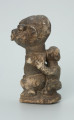 rzeźba; przedmiot obrzędowy; Figura kultu sił wegetacji - Ujęcie lewy bok. Rzeźbiona w grafitowym steatycie siedząca postać ludzka o cechach kobiecych z podkurczonymi nogami i dzieckiem na plecach.