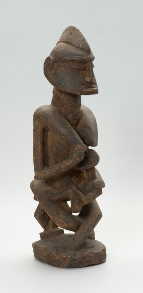 drewniana, rzeźbiona figura - Ujęcie z przodu, z prawej strony. Drewniana, rzeźbiona postać kobiety, trzymającej w ramionach małe dziecko.