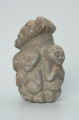 rzeźba; przedmiot obrzędowy; figura kultu zmarłych - Ujęcie lewy bok. Rzeźba o gładkiej powierzchni w szarym steatycie, przedstawiająca postać ludzką o cechach kobiecych, otoczoną piątką mniejszych, dziecięcych sylwetek w różnych pozach.