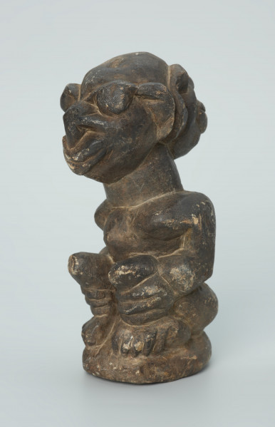 rzeźba; przedmiot obrzędowy; Figura kultu sił wegetacji - Ujęcie z przodu z lewej strony. Rzeźbiona w grafitowym steatycie siedząca postać ludzka o dwóch twarzach, z przodu i z tyłu głowy.