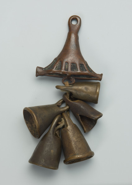biżuteria, ozdoba - Ujęcie z tyłu. Mały, trójkątny, ozdobiony wzorami geometrycznymi wisiorek, wykonany z brązu, z którego zwisa pięć dzwoneczków umieszczonych na bawełnianym sznurku.