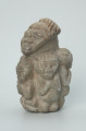 rzeźba; przedmiot obrzędowy; figura kultu zmarłych - Ujęcie z przodu z lewej strony. Rzeźba o gładkiej powierzchni w szarym steatycie, przedstawiająca postać ludzką o cechach kobiecych, otoczoną piątką mniejszych, dziecięcych sylwetek w różnych pozach.