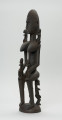 drewniana figura - Ujęcie z przodu, z prawej strony. Drewniana, rzeźbiona figura kobiety. Na jej ramionach i rękach znajdują się mniejsze figurki.