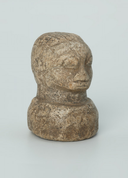 rzeźba; przedmiot obrzędowy; Głowa - Ujęcie z przodu z prawej strony. Rzeźbiona w szarobeżowym steatycie głowa ludzka na okrągłej podstawie z charakterystycznym uczesaniem lub nakryciem głowy w formie płaskiego ornamentu kostkowego.