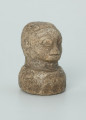rzeźba; przedmiot obrzędowy; Głowa - Ujęcie z przodu z prawej strony. Rzeźbiona w szarobeżowym steatycie głowa ludzka na okrągłej podstawie z charakterystycznym uczesaniem lub nakryciem głowy w formie płaskiego ornamentu kostkowego.