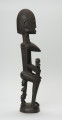 drewniana figura - Ujęcie z lewego boku. Drewniana, rzeźbiona figura kobiety. Na jej ramionach i rękach znajdują się mniejsze figurki.